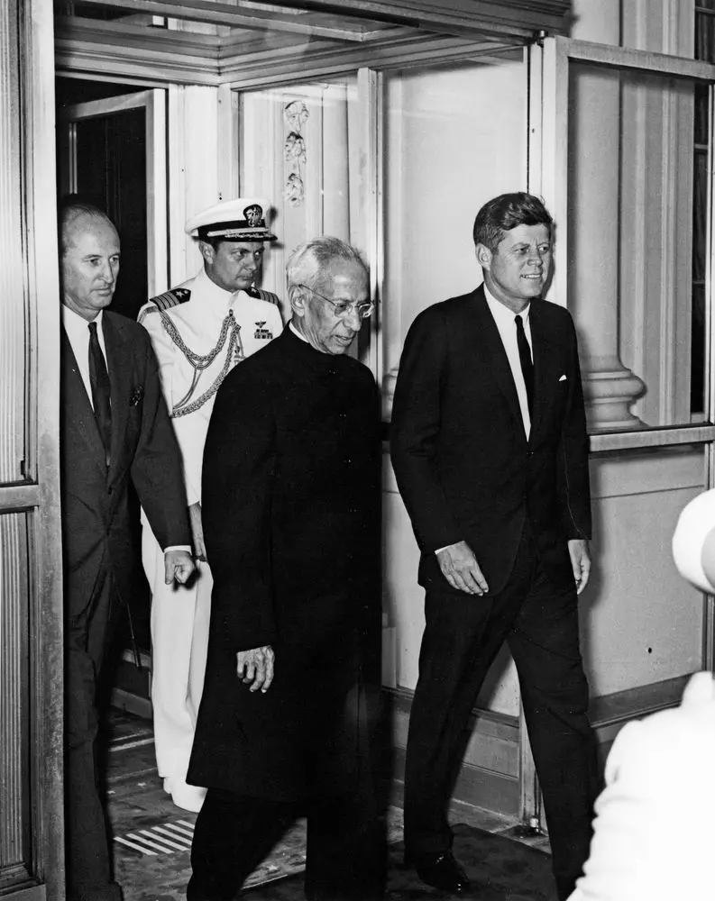 "Dr. Sarvepalli Radhakrishnan walking alongside U.S. President John F. Kennedy, accompanied by officials and a naval officer, during a formal visit.