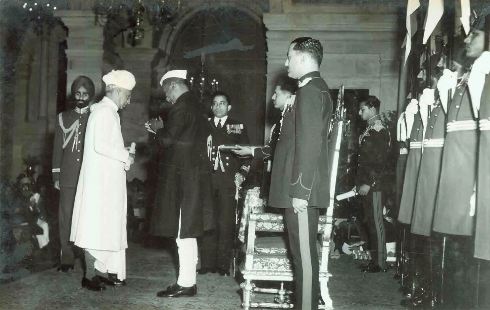 Dr. Sarvepalli Radhakrishnan, dressed in white traditional attire and turban, presenting an award to a man during a formal ceremony, with military officers and guards in uniform standing nearby.