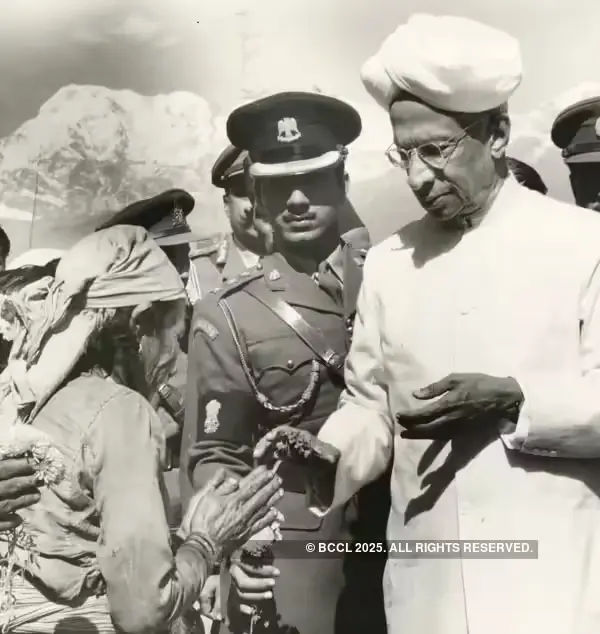 "Dr. Sarvepalli Radhakrishnan, wearing a white turban and traditional attire, receiving a garland from a woman, with army officers standing behind him and mountains in the background.