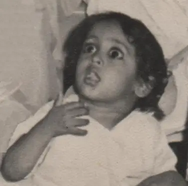 Black-and-white photograph of a young child with wide, expressive eyes, looking upward in surprise or curiosity, wearing a light-colored outfit.