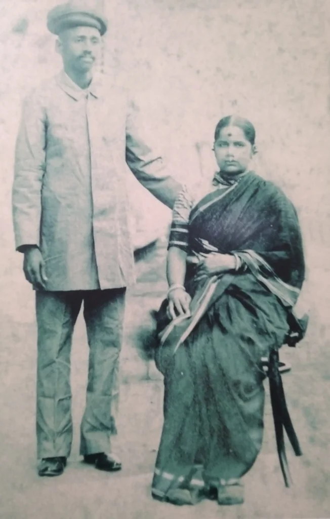 Maharshi Dhondo Keshav Karve standing beside his wife Anandibai (also known as Baya Karve), both dressed in traditional Indian attire, posed formally against a plain backdrop.