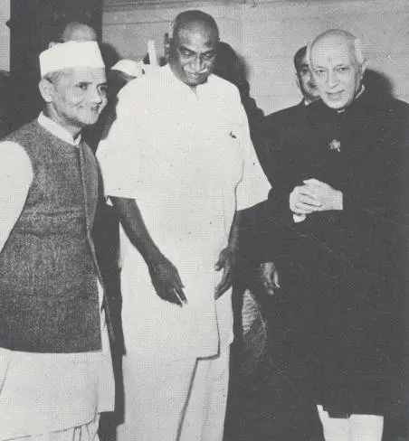 Jawaharlal Nehru on the left, wearing a Gandhi cap and Nehru jacket; Lal Bahadur Shastri at center, dressed in a simple kurta; and K. Kamaraj on the right, in traditional attire. They appear posed in a formal setting before 1955.