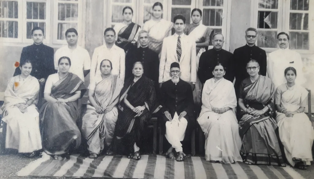 Maharshi Dhondo Keshav Karve surrounded by his family—men, women, and children—standing and seated in traditional early 20th-century Indian attire, posed formally against a simple interior or exterior backdrop.