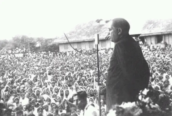 Dr. B. R. Ambedkar delivering a speech, captured from a distance, with a large crowd gathered around him.