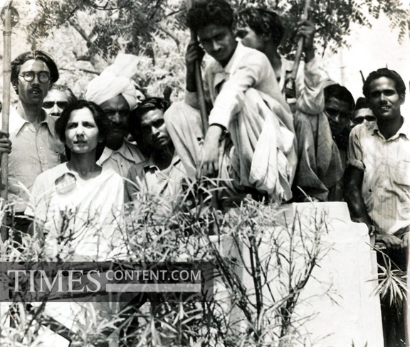  Aruna Asaf Ali wearing a sari and glasses, speaking into multiple microphones at a public event.