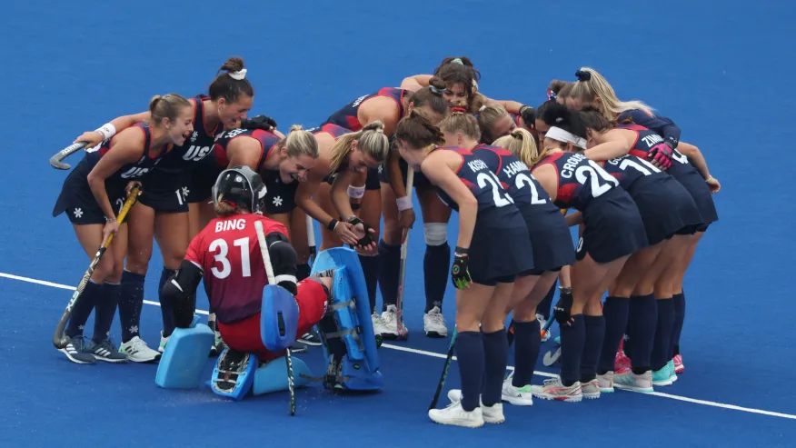 The USA women's field hockey team in a tight huddle on the blue turf before a game.