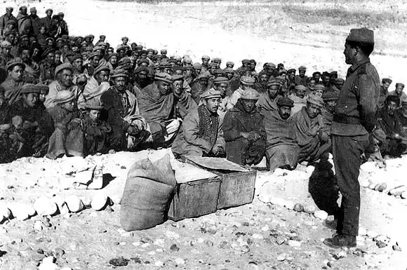 Black-and-white photograph of Indian soldiers seated in a cold mountainous area, listening to an officer addressing them.
