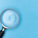 Close-up of a magnifying glass on a blue surface, ideal for search and exploration themes.